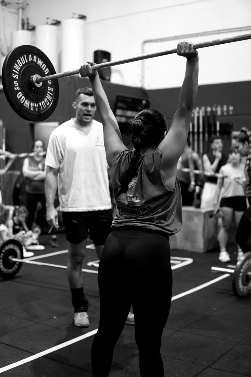 Atleta sosteniendo una barra sobre la cabeza mientras un coach observa en CrossFit Sant Boi