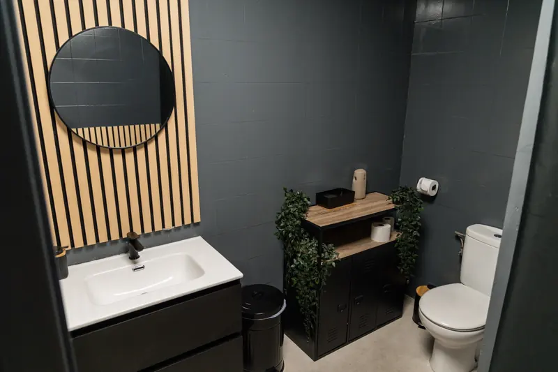 Vestuario con lavabo, espejo redondo y pared de listones de madera